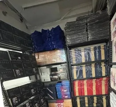 Warehouse shelves stacked with boxed stock and packed goods, the stage a parcel sits at before a Novaluxia delivery update appears in the app